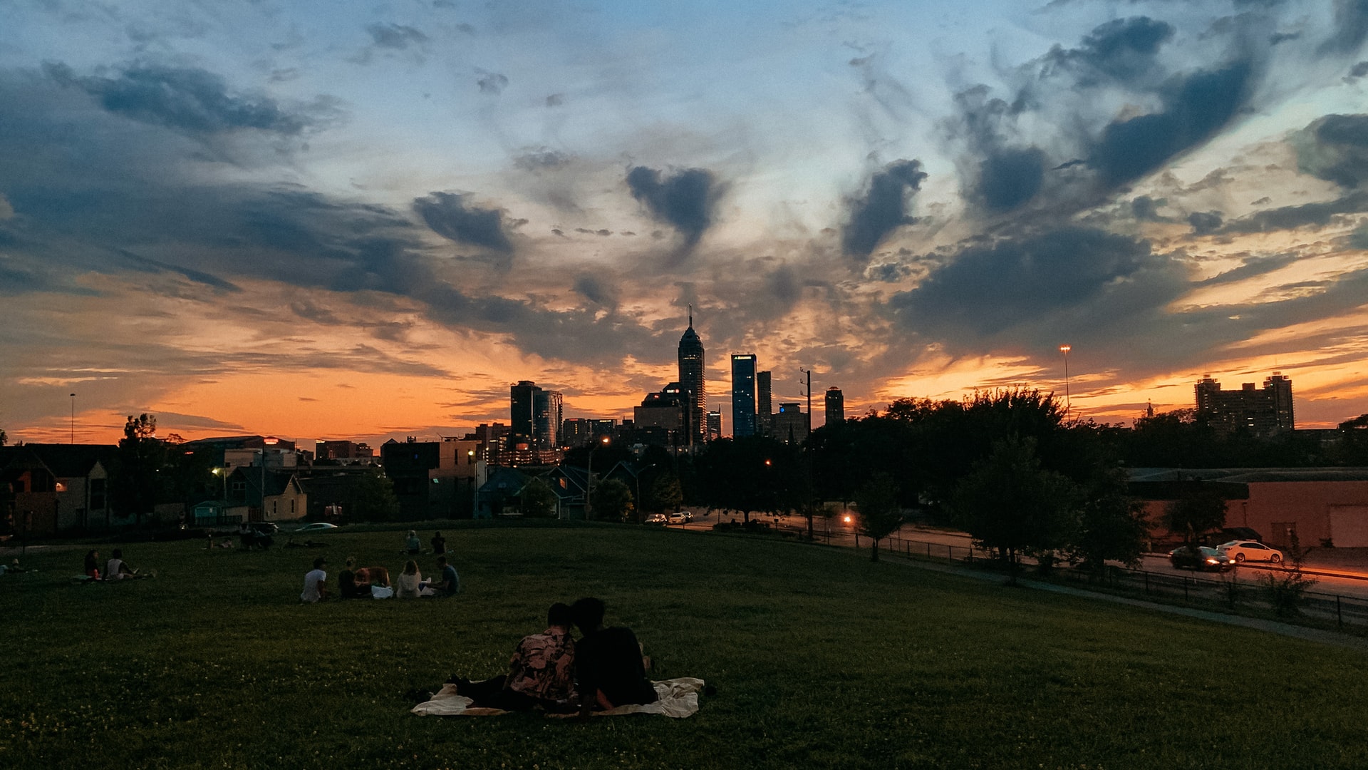 People sitting in a park looking at a skyline of Indianapolis at sunset.