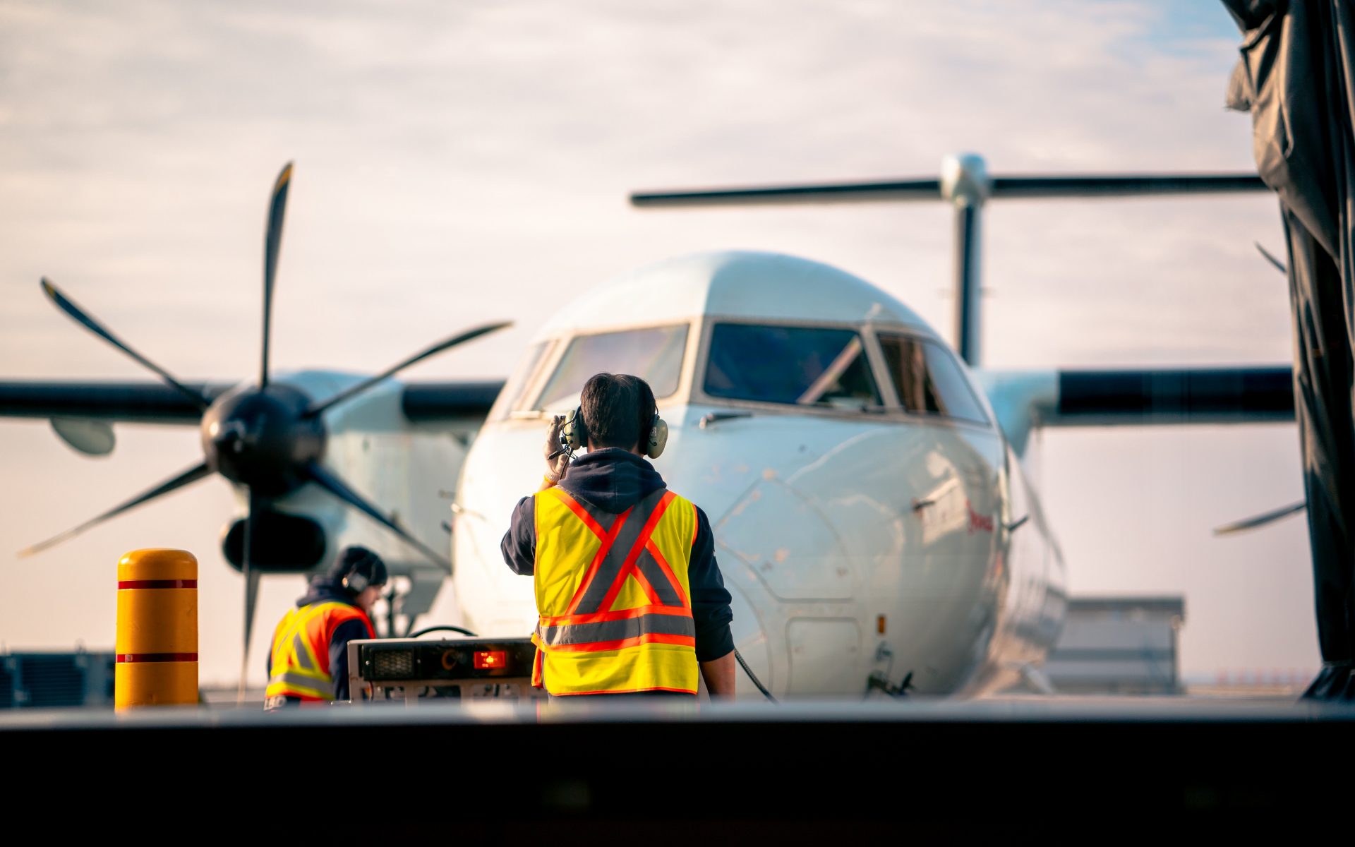 Person in yellow vest stands in front of a parked airplane.